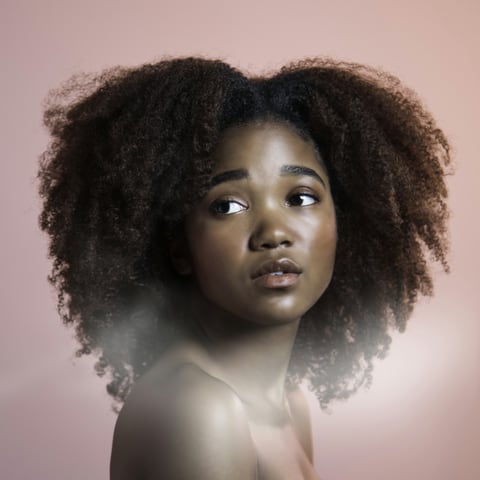 Portrait of a woman with natural curly hair against a soft pink background